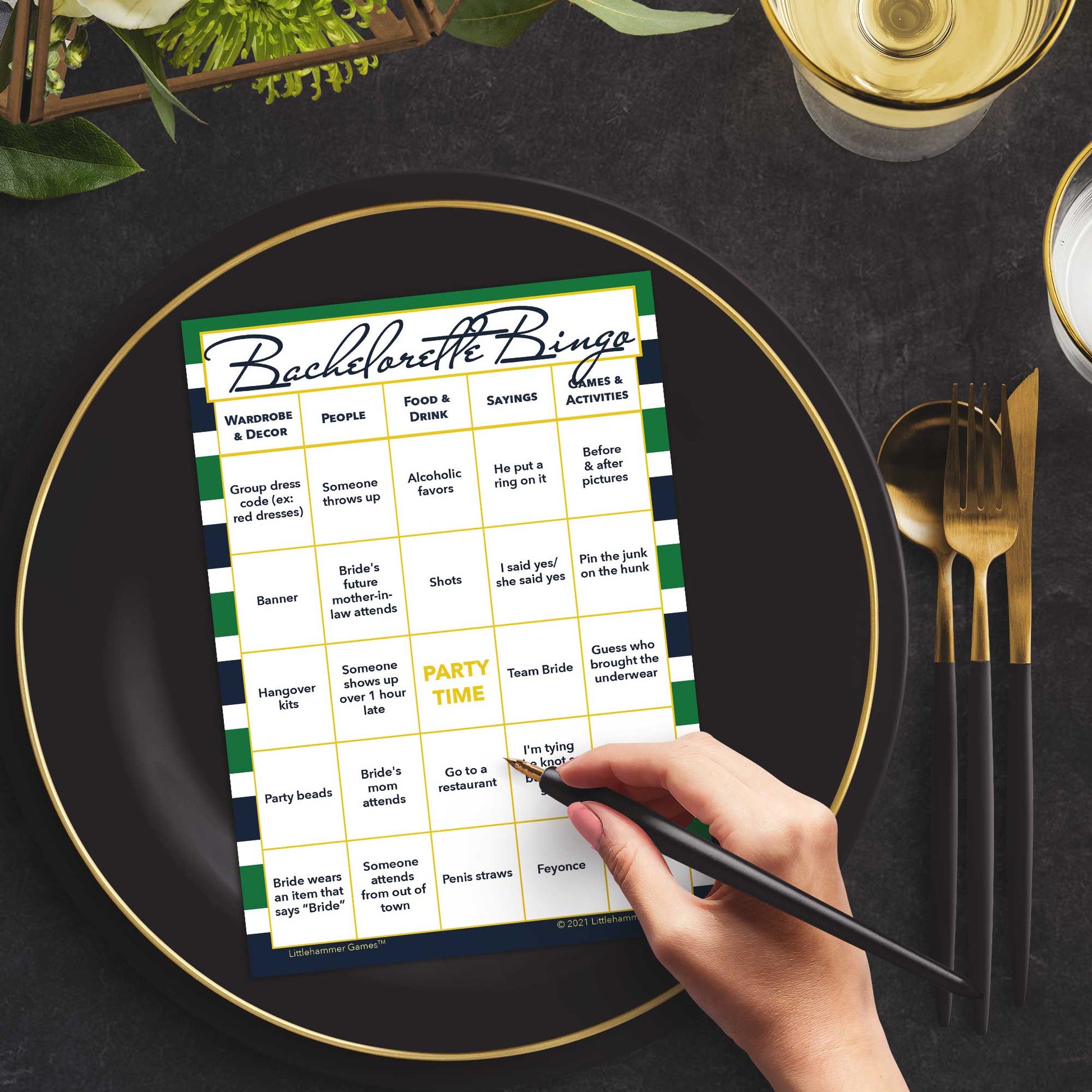 Woman with a pen sitting at a table with a green and navy-striped Bachelorette Bingo game card on a gold and black plate on a dark place setting