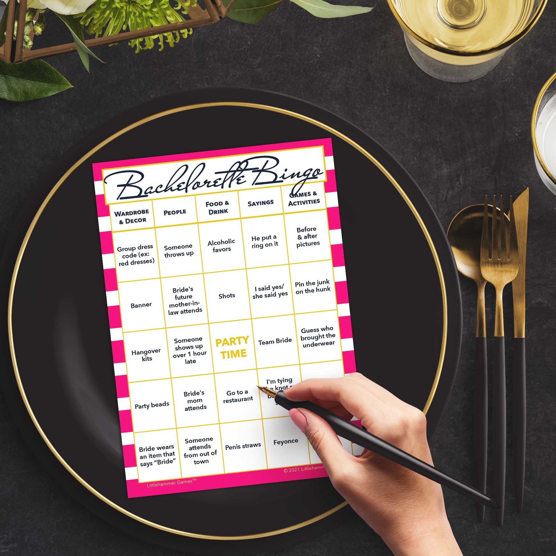 Woman with a pen sitting at a table with a hot pink-striped Bachelorette Bingo game card on a gold and black plate on a dark place setting