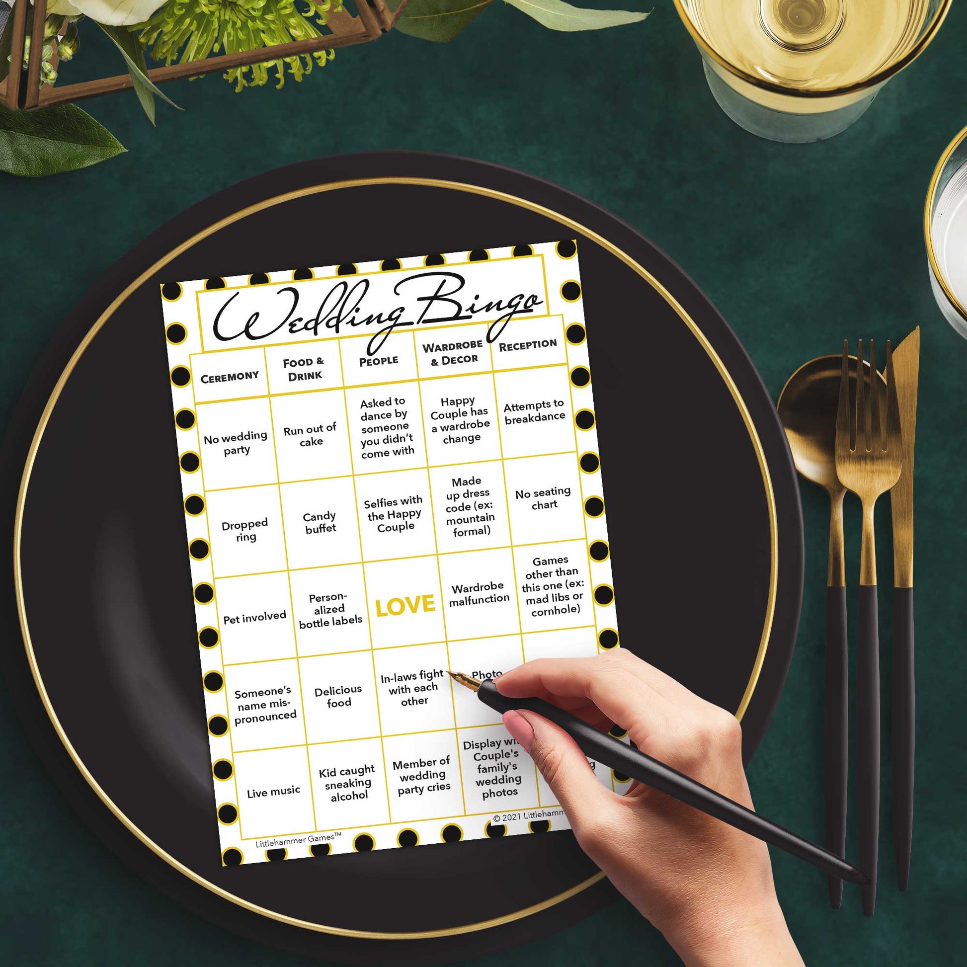 Woman with a pen sitting at a table with a black and gold polka dot Wedding Bingo game card on a black and gold plate at a dark place setting