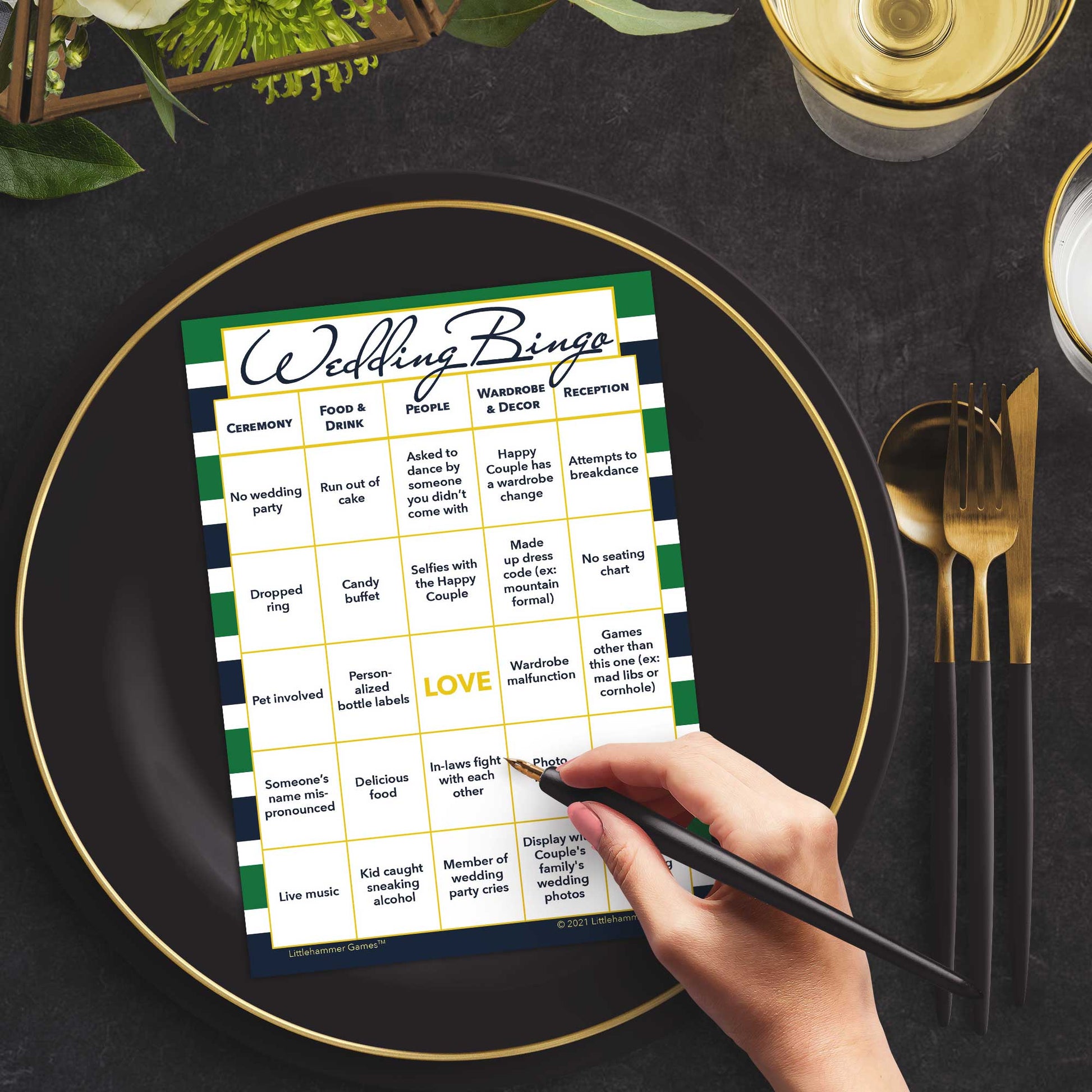 Woman with a pen sitting at a table with a green and navy-striped Wedding Bingo game card on a black and gold plate at a dark place setting