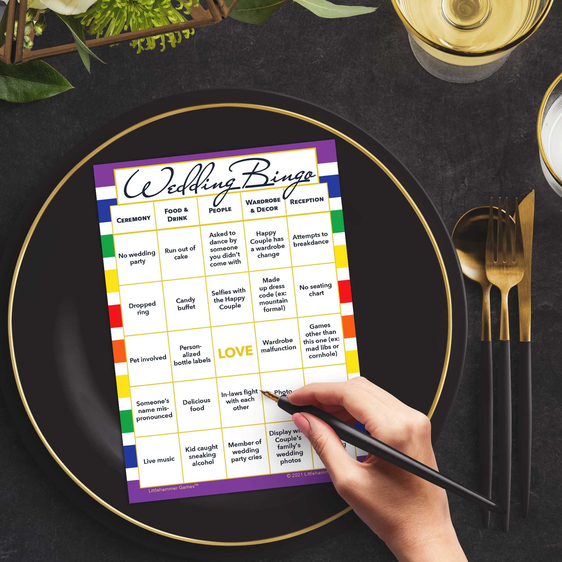 Woman with a pen sitting at a table with a rainbow-striped Wedding Bingo game card on a black and gold plate at a dark place setting